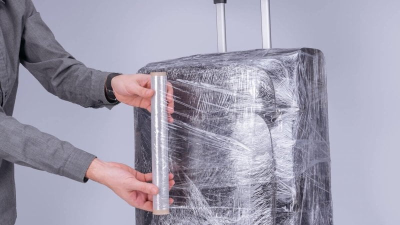 Homem no final do processo de envelopar mala de viagem preta