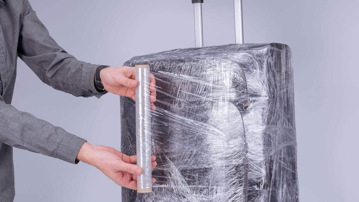 Homem no final do processo de envelopar mala de viagem preta